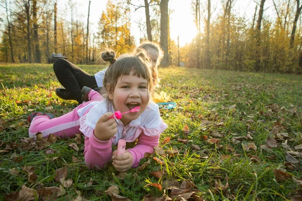 Dos hermanas en el parque de otoño - una niña tendida en el suelo y soplando burbujas de jabón — Foto de Stock