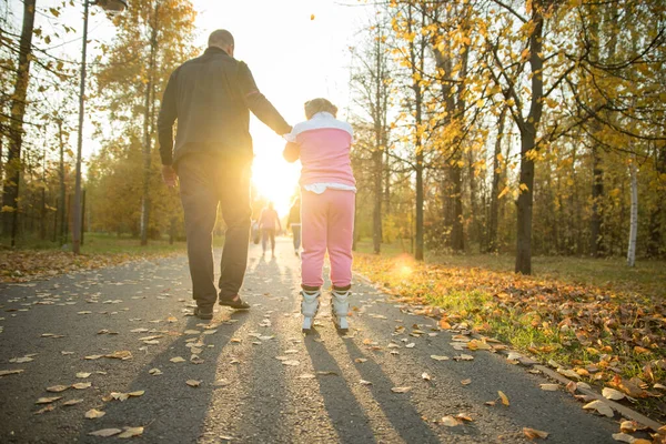 Счастливая семья отца и его дочь, гуляющие в парке - девушка, катающаяся на роликах — стоковое фото
