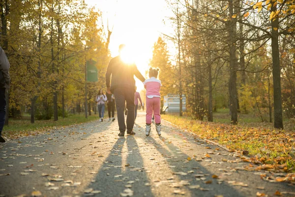 Gelukkige familie van vader en zijn dochter wandelen in de herfst park - het meisje rijden op de rollen — Stockfoto