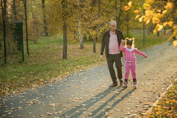 Famiglia di papà e sua figlia che camminano nel parco autunnale - la ragazza che cavalca sui rulli — Foto Stock