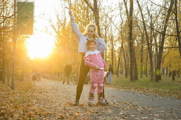 Due sorelle che camminano nel parco autunnale - una bambina che cavalca sui rulli — Foto Stock