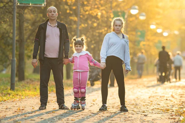 Gelukkige familie van vader en zijn twee dochters wandelen in de herfst park - een klein meisje rijden op de rollen — Stockfoto