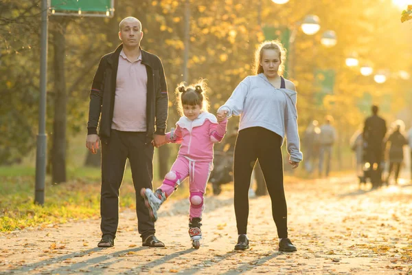 Familie van vader en zijn twee dochters wandelen in het najaar park - een klein meisje rijden op de rollen — Stockfoto