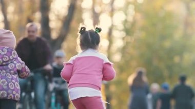 Sonbahar parkında küçük bir scooter süren pembe kostümlü küçük bir kız.