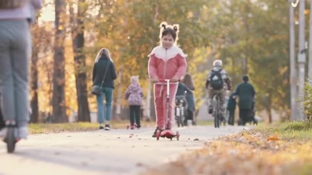 Een meisje in roze kostuum paardrijden een kleine scooter in de herfst park — Stockvideo
