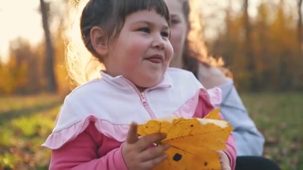 Two sisters spending time and fooling around in autumn park - little one playing with a leaf — Stock Video