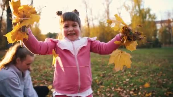 To smilende søstre tilbringer tid i høstparken og samler appelsinblader – stockvideo