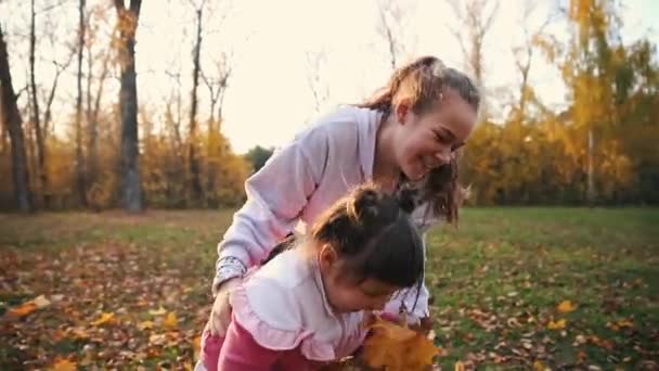 Дві усміхнені сестри проводять час і обманюють осінній парк і збирають апельсинове листя — стокове відео