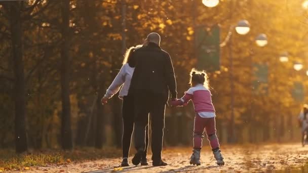 Сім'я тата і його дві дочки гуляють в парку - маленька дівчинка катається на роликах — стокове відео