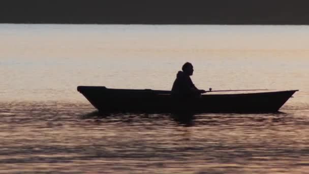 Hombre sentado en un barco y pescando al atardecer — Vídeo de stock