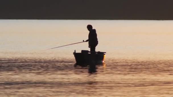 Een silhouet van de mens zittend in een boot en vissen op de zonsondergang — Stockvideo