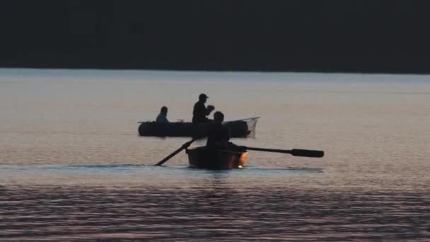 Silhouetten van mannen die in een boot zitten en bij zonsondergang vissen — Stockvideo