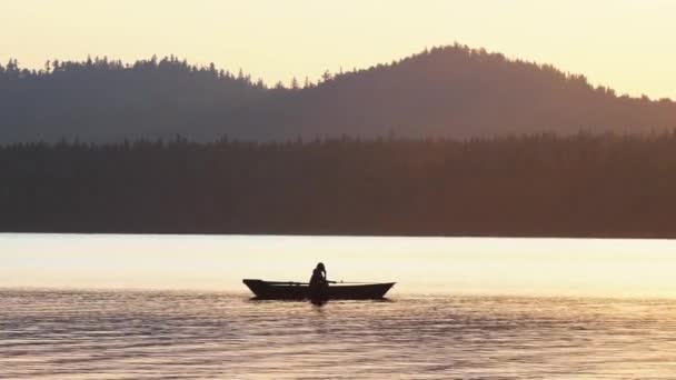 Una silueta de hombre sentado en un barco y pescando en la naturaleza mientras el atardecer — Vídeo de stock