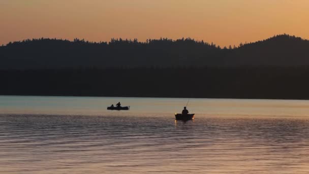 Una silueta de personas sentadas en un barco y pescando en la naturaleza mientras el atardecer — Vídeos de Stock