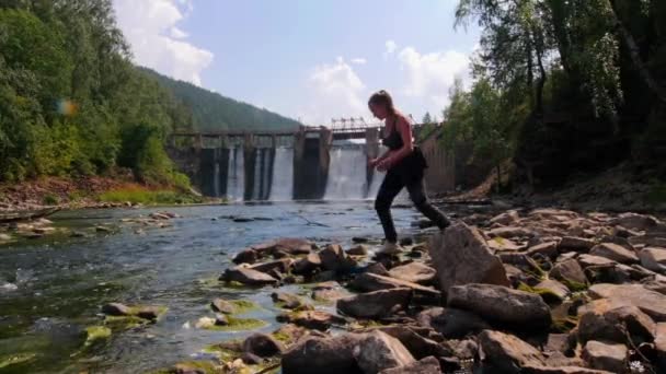 休暇中の若い女性-ストリーミング水の近くの岩の上を歩く — ストック動画