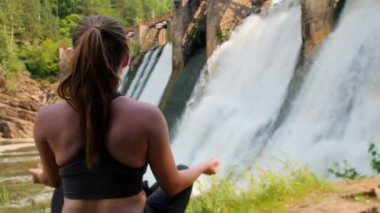 Tatilde olan genç bir kadın barajın yanında yoga yapıyor.