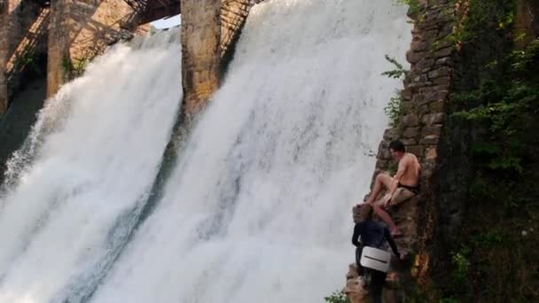 Een paar op vakantie - man en vrouw kijken naar het water valt van de dam — Stockvideo