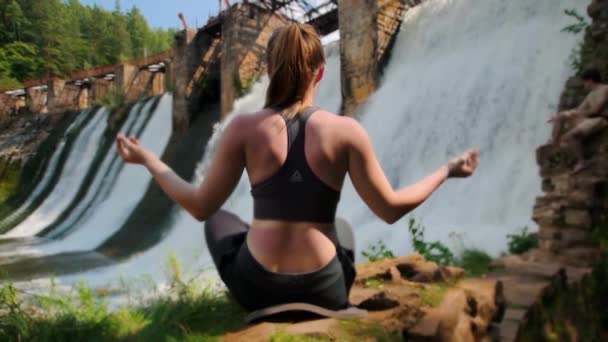 Młoda kobieta na wakacjach uprawia jogę w pobliżu tamy wodnej - medytuje — Wideo stockowe