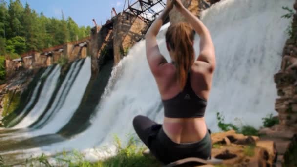 Młoda kobieta na wakacjach uprawia jogę w pobliżu tamy wodnej w lesie - medytuje — Wideo stockowe