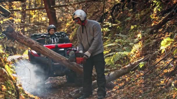 Un hombre enciende una motosierra en el bosque y su hijo lo está esperando en una quad bike — Vídeo de stock