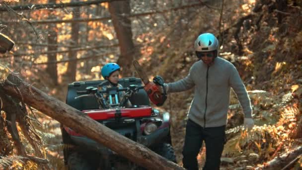 Un bosque otoñal: el hombre toma una motosierra y su hijo lo espera en una bicicleta cuádruple — Vídeo de stock