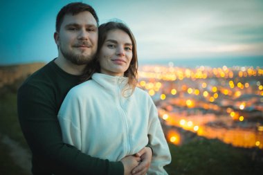 Arka planda güzel bir şehir manzarası olan bir tepede kucaklaşan romantik çift.