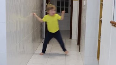 Genç çocuk fayanslı bir koridorda çıplak ayakla dans etmekten zevk alıyor, hareket yoluyla neşe ve özgürlüğü ifade ediyor.