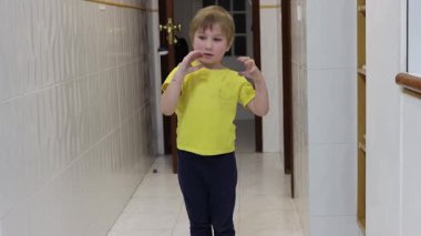 Enerjik çocuk koridorda dans ediyor, müzikten hoşlanıyor ve hareketlerle kendini ifade ediyor.