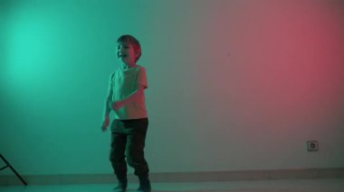 Enerjik çocuk, gök mavisi ve kırmızı sahne ışıkları altında çeşitli dans hareketleri yapar.