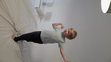 Sarışın çocuk yatakta zıplarken ve oynarken eğleniyor.