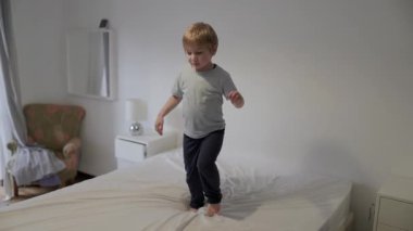 Sarışın çocuk yatakta zıplayıp oynamaktan hoşlanıyor.