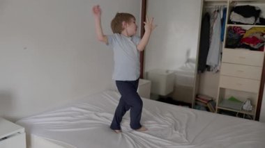 Mutlu çocuk yatak odasında yatakta zıplarken eğleniyor.