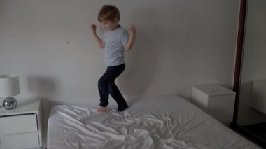 Çocuk yatakta zıplıyor ve dans ediyor.