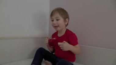 Kırmızı meyve suyu içen ve ekmek yiyen mutlu bir çocuk beyaz bir zemin üzerinde düz bir zemin üzerinde oturuyor.