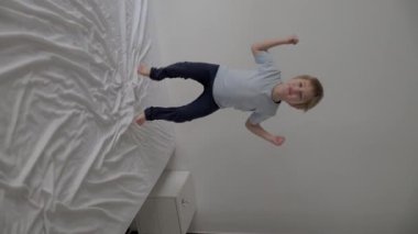 Mutlu çocuk enerjik bir şekilde zıplıyor ve bir yatakta oynuyor, oyun zamanının tadını çıkarıyor.
