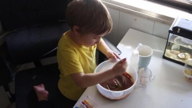 Konsantre çocuk, malzemeleri bir kaseye dikkatlice karıştırıyor ve lezzetli bir ziyafet hazırlıyor.