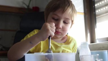 Sarışın çocuk mutfakta çikolatalı krema yiyor.