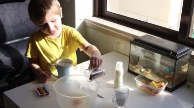 Çocuk kaseye çikolata tozu ekliyor, çikolatalı süt içeceği hazırlıyor.