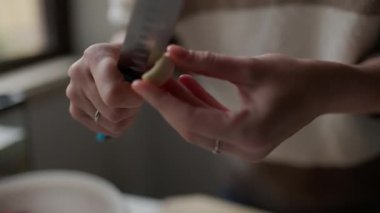 Kadın aşçı, bir yemek tarifi için sarımsak hazırlıyor, ahşap bir kesme tahtasıyla soyup kıyma yapıyor.