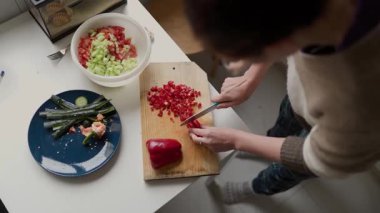 Ahşap bir kesme tahtasında kırmızı biber dilimleyen bir kadın, mutfağında sağlıklı bir yemek hazırlıyor.