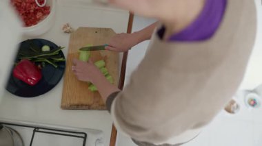 Ev aşçısı, parlak bir mutfakta, ahşap bir kesme tahtasının üzerinde kereviz dilimler.