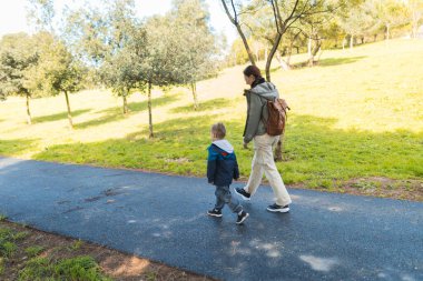 Anne ve oğul güneşli bir parkta keyifli bir gezinti yapıyorlar, doğada birlikte güzel vakit geçiriyorlar.