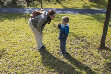 Anne, güneşli bir günde oğlunu dinlemek için eğiliyor ve birlikte güzel vakit geçiriyor.