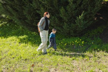 Güneşli bir günde parkta yürüyüş yapan anne ve oğul.