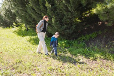 Anne ve oğlu ormanın yakınındaki çimenli bir tarlada yürüyor, manzaranın ve temiz havanın tadını çıkarıyorlar.