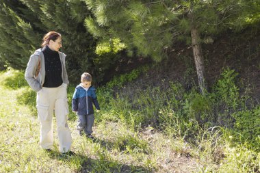 Anne ve oğlu yemyeşil yemyeşil bir orman patikasında sakin bir şekilde yürüyor.