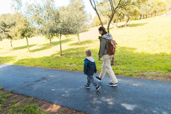 Anne ve oğul güneşli bir parkta keyifli bir gezinti yapıyorlar, doğada birlikte güzel vakit geçiriyorlar.