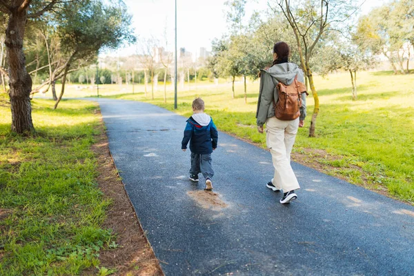 Anne ve oğlu canlı yeşil bir parkta keyifli bir gezinti yapıyorlar. Birlikte güzel vakit geçiriyorlar.
