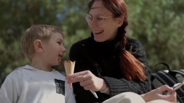 Anne ve oğlu parktaki bankta çikolatalı dondurmanın tadını çıkarıyorlar.