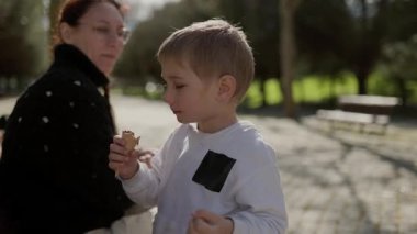 Parkta annesiyle dondurma külahı yiyen mutlu çocuk.